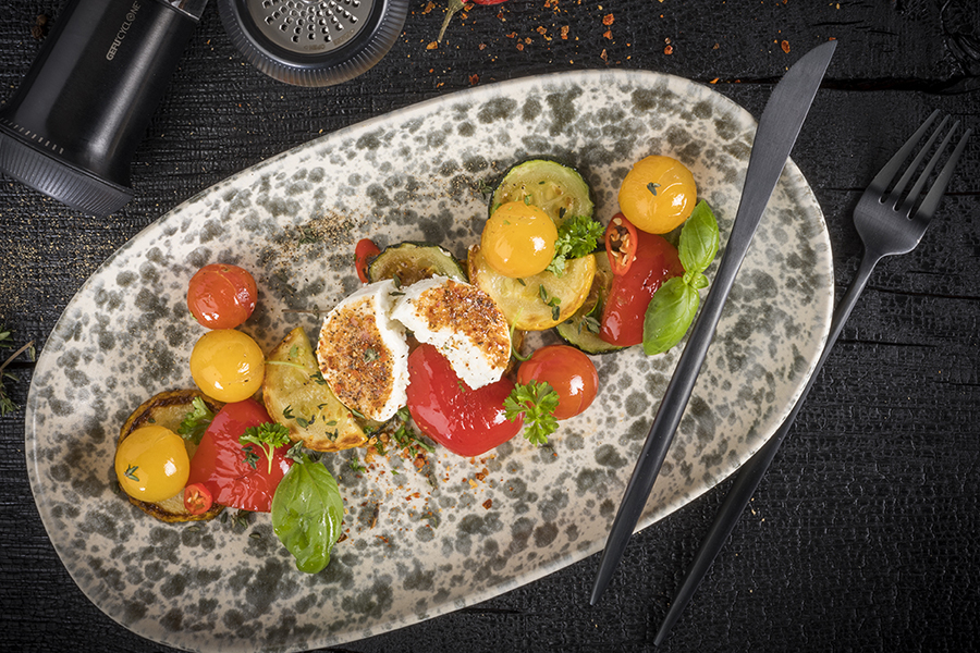 Antipasti mit Ziegenkäse unter einer Pfeffer-Chili Kruste Keramikteller mit gegrilltem Gemüse, gelben und roten Tomaten sowie gebackenem Mozzarella, dekoriert mit frischen Kräutern