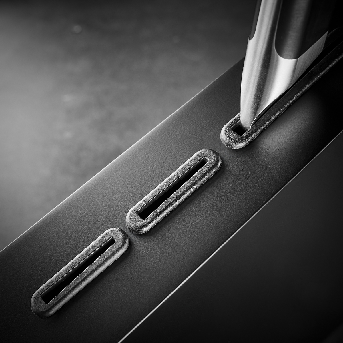 Ein Metallwerkzeug platziert in einem schmalen Schlitz auf der Oberfläche eines schwarzen Geräts, das für technische Präzision genutzt wird.