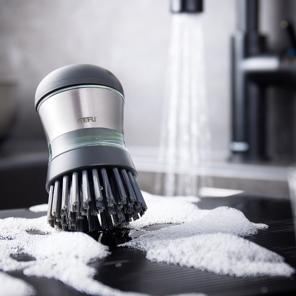 Spülbürste mit Spülmittelspender SWIFT von GEFU beim Abwaschen auf nasser, schaumiger Oberfläche in der Küche