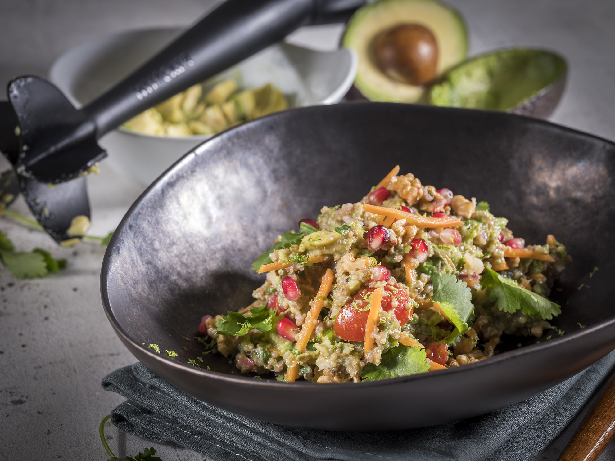 Quinoa-Avocado-Salat mit Granatapfelkernen und Walnüssen  Nahaufnahme eines frischen Quinoa-Salats mit Avocado, Granatapfelkernen und Koriander in einer schwarzen Schüssel