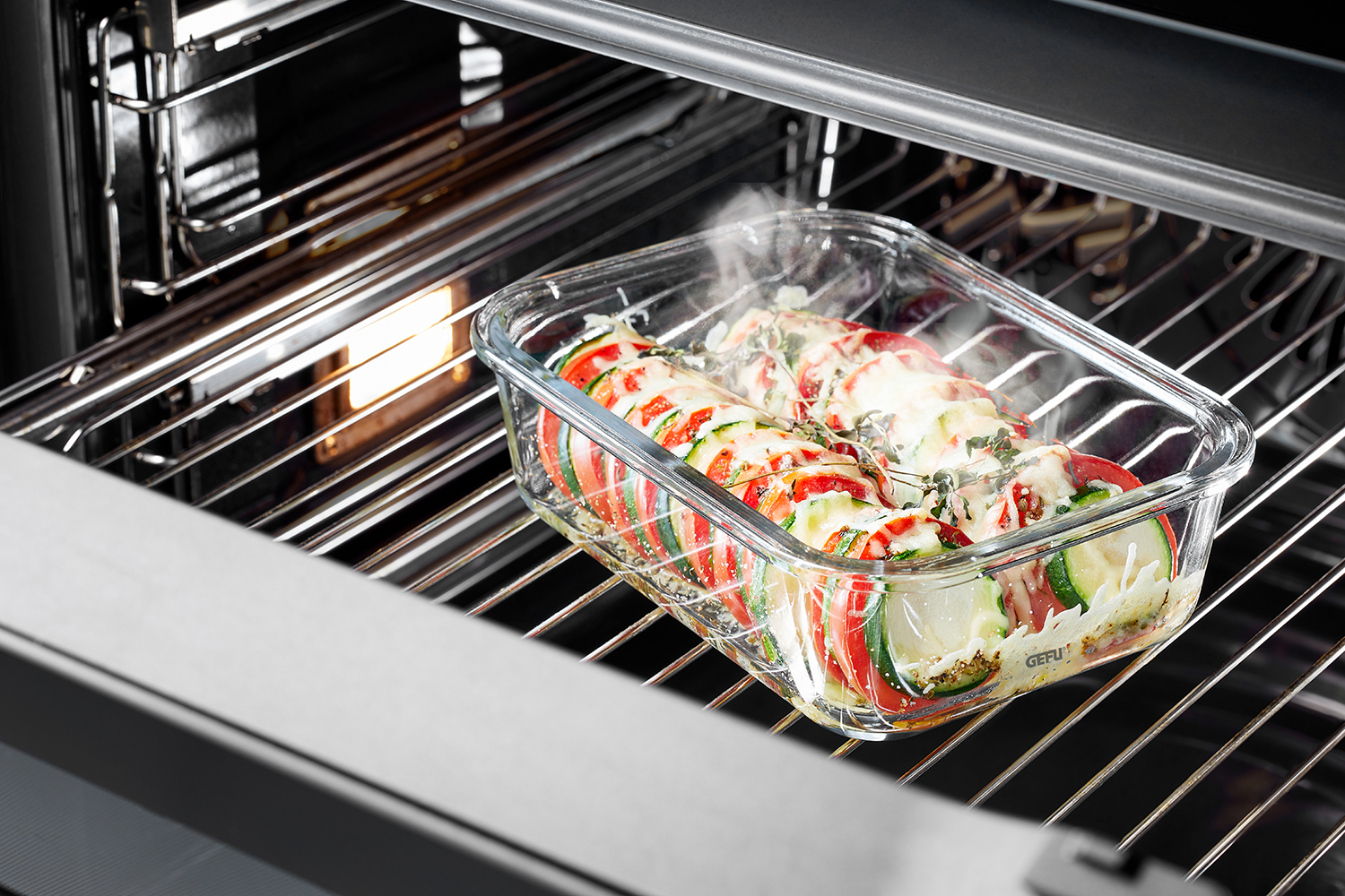 Frisch zubereiteter Gemüseauflauf im Ofen gebacken Ein dampfender Gemüseauflauf in einer Glasauflaufform im Ofen, bestehend aus Tomaten, Zucchini und Käse