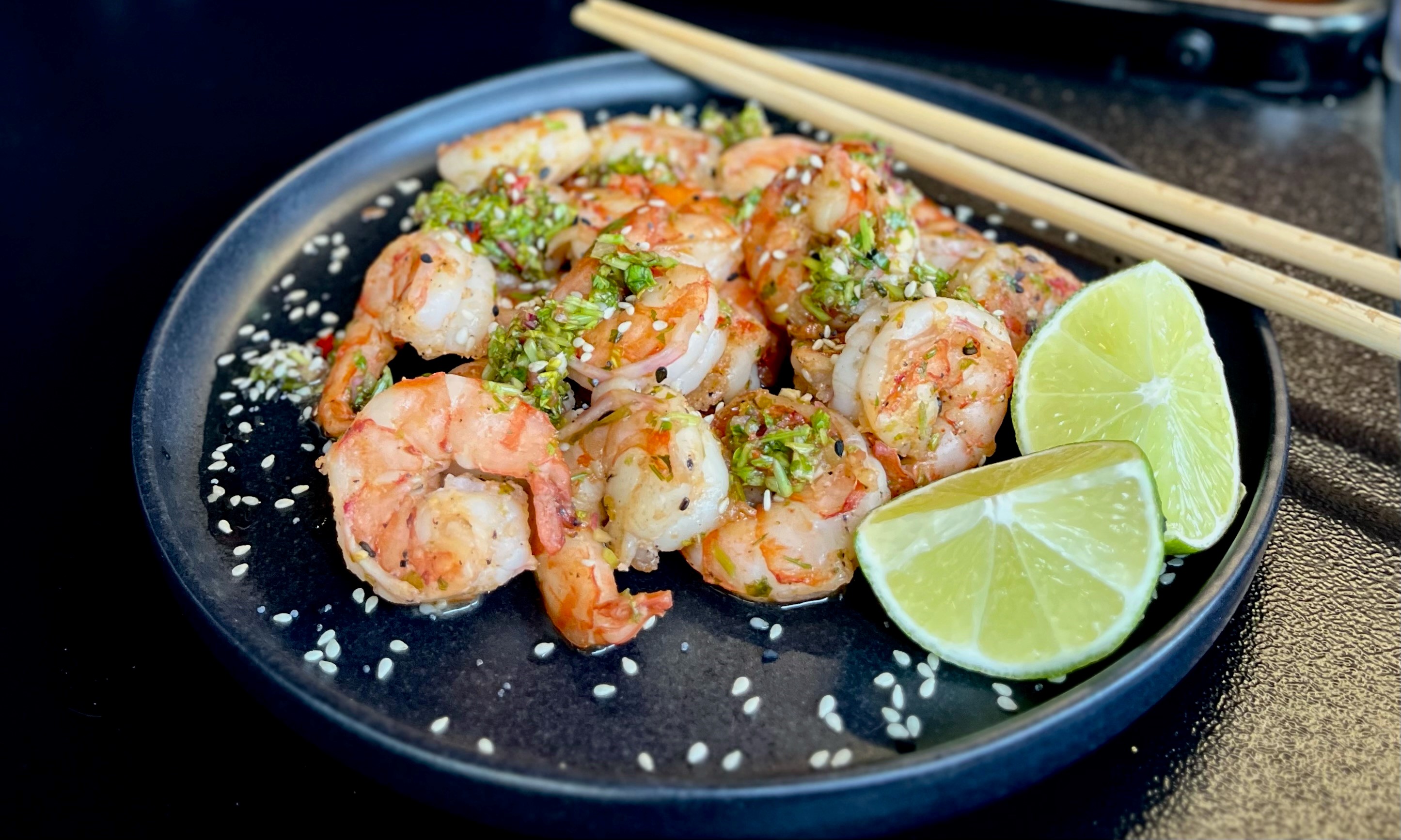Black Tiger Prawns mit Nam Jim Dip  Nahaufnahme eines Garnelengerichts mit Limettenscheiben und Sesam, serviert auf einem schwarzen Teller mit Essstäbchen