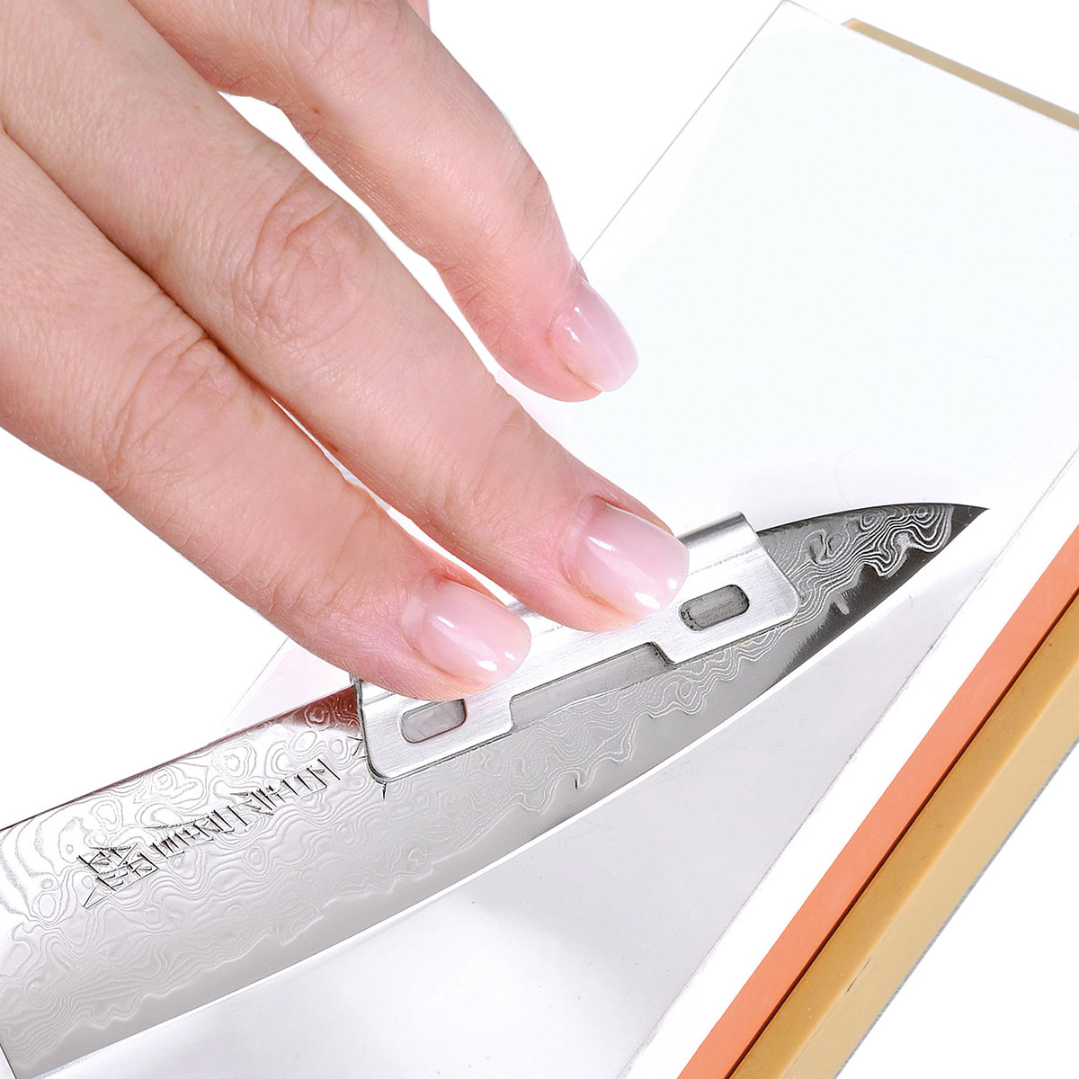 Damastmesser wird auf einem Schleifstein geschärft Nahaufnahme einer Hand, die ein Damastmesser auf einem Schleifstein schärft