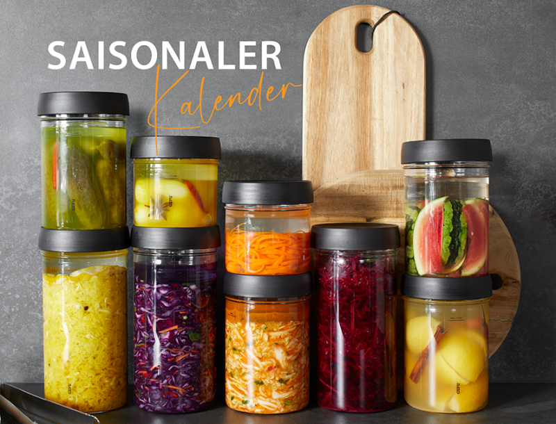 Saisonaler Kalender für eingelegtes Gemüse in Gläsern Verschiedene Gläser mit eingelegtem Gemüse vor Holzhintergrund, beschriftet mit 'Saisonaler Kalender'.