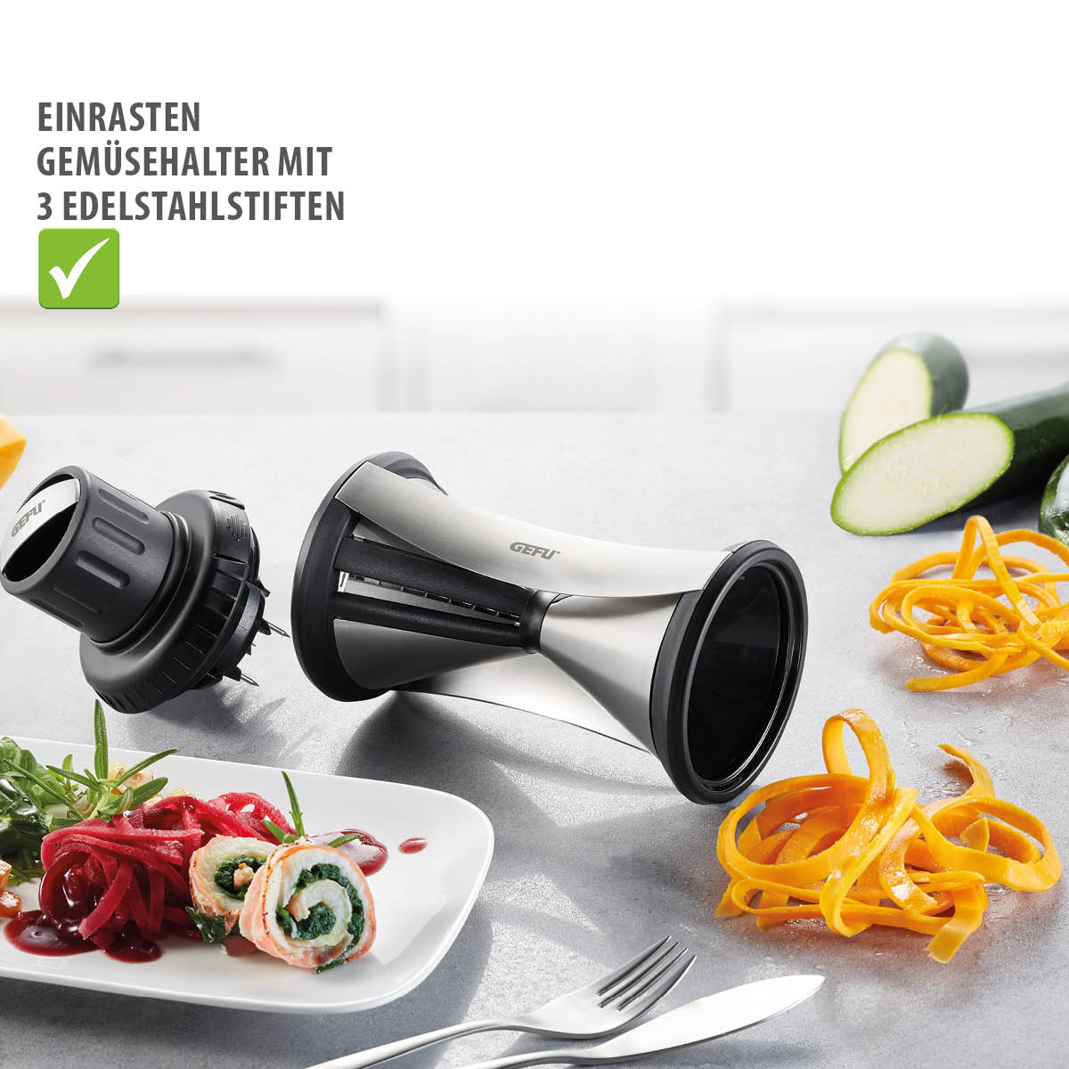 Spiralschneider mit Gemüsehalter und Edelstahlstiften für kreative Gerichte Spiralschneider mit Einrast-Gemüsehalter, Zucchini und Karottennudeln auf einer Arbeitsfläche