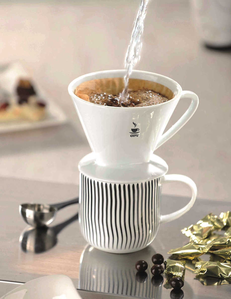 Weißer Kaffeebereiter auf gestreifter Keramiktasse, Wasser wird eingegossen