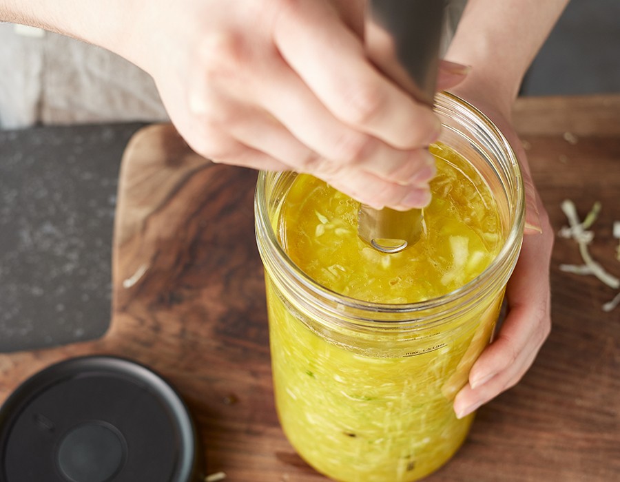 Goldenes Sauerkraut  Nahaufnahme von Händen, die ein Glas mit fermentierendem Gemüse umrühren