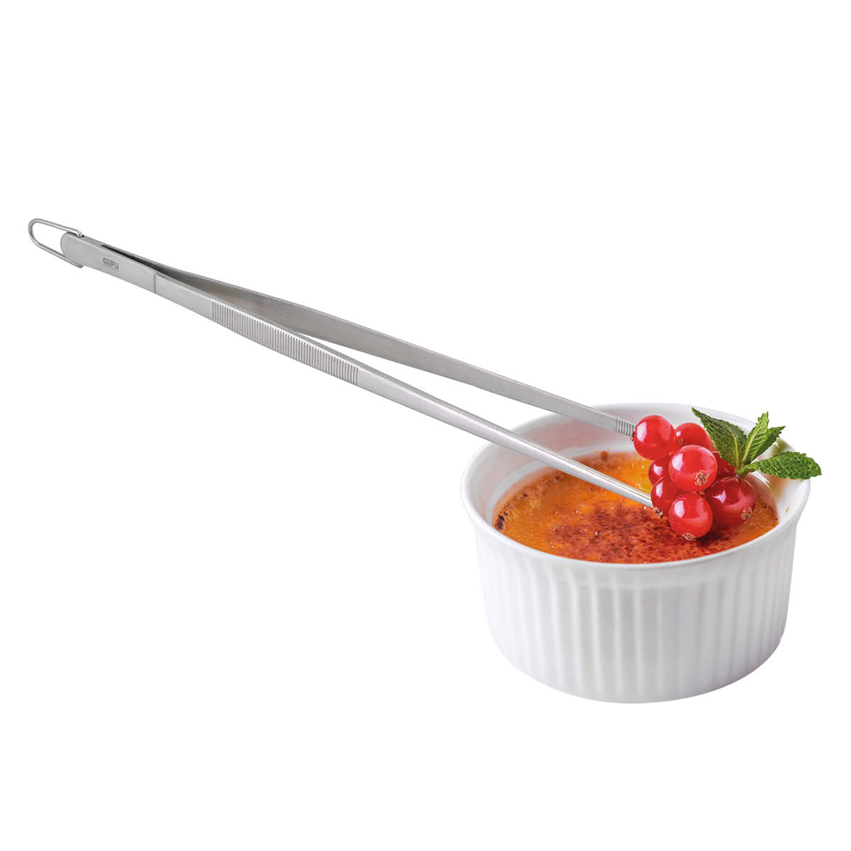 Edelstahl-Kochpinzette mit Crème Brûlée und Dekoration Edelstahl-Kochpinzette hält Johannisbeeren und Minze auf Crème Brûlée in einer weißen Schale