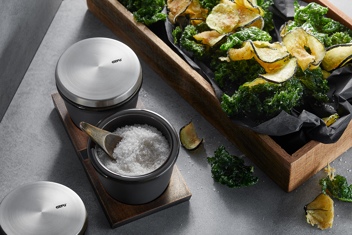 Elegantes Salzschälchen-Set mit holzverzierter Ablage Salzschälchen aus Edelstahl mit Holzlöffel und Gemüsechips auf einem Tisch