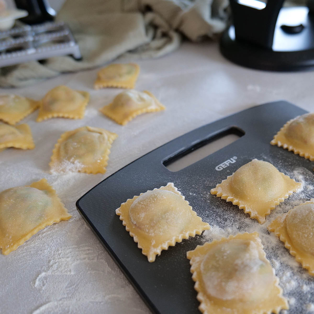 Frische hausgemachte Ravioli auf einem Ravioli-Brett Mehrere frische, ungekochte Ravioli auf einem Ravioli-Brett und einem bemehlten Tisch