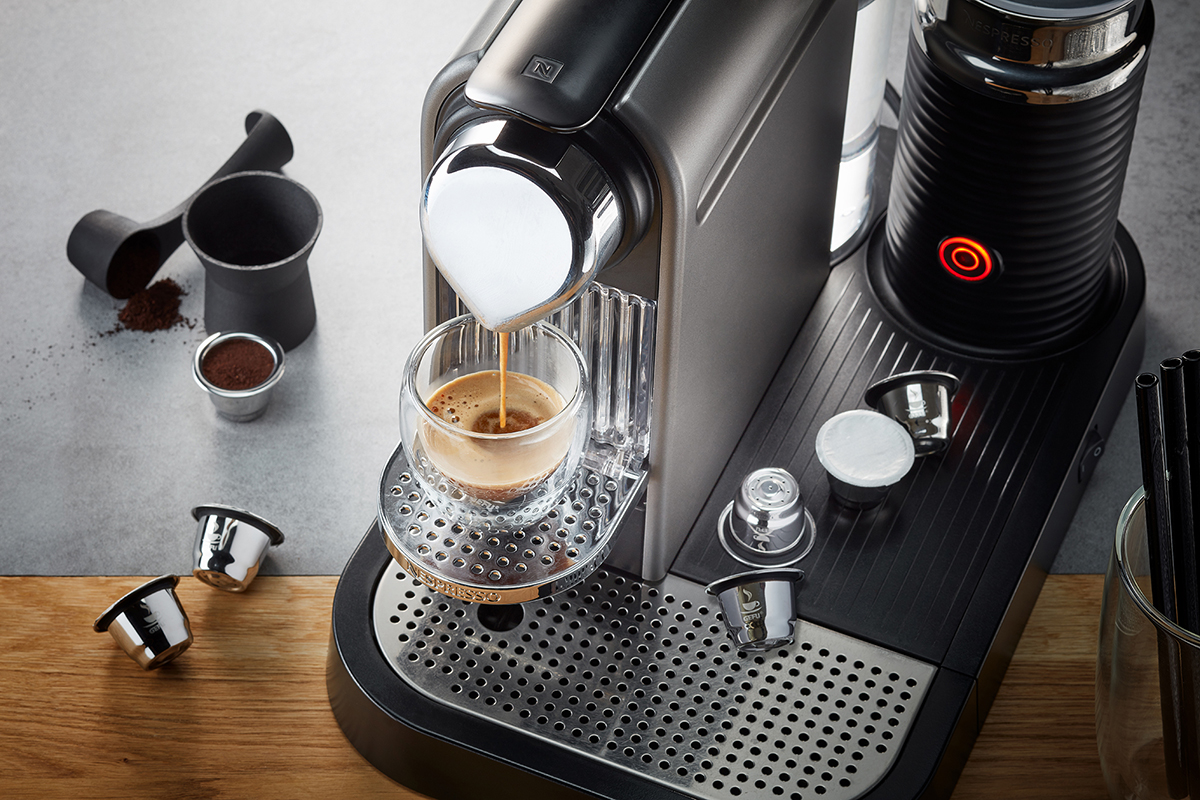 Espressomaschine mit Glas, das frisch gebrühten Espresso auffängt, umgeben von Kaffeekapseln
