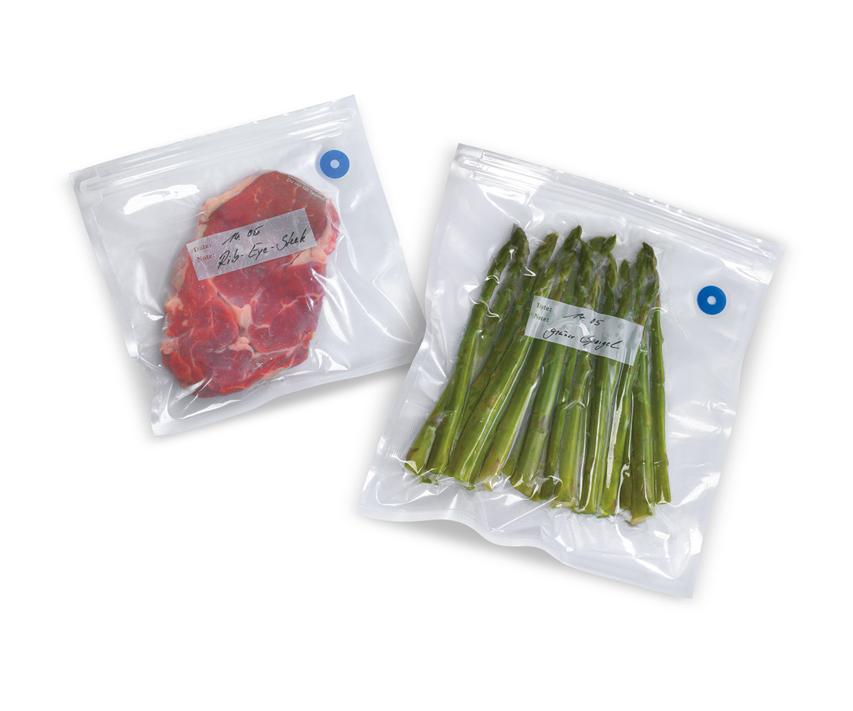 Vakuumverpacktes Rib-Eye-Steak und grüner Spargel in Beuteln Zwei vakuumverpackte Beutel mit Rib-Eye-Steak und grünem Spargel