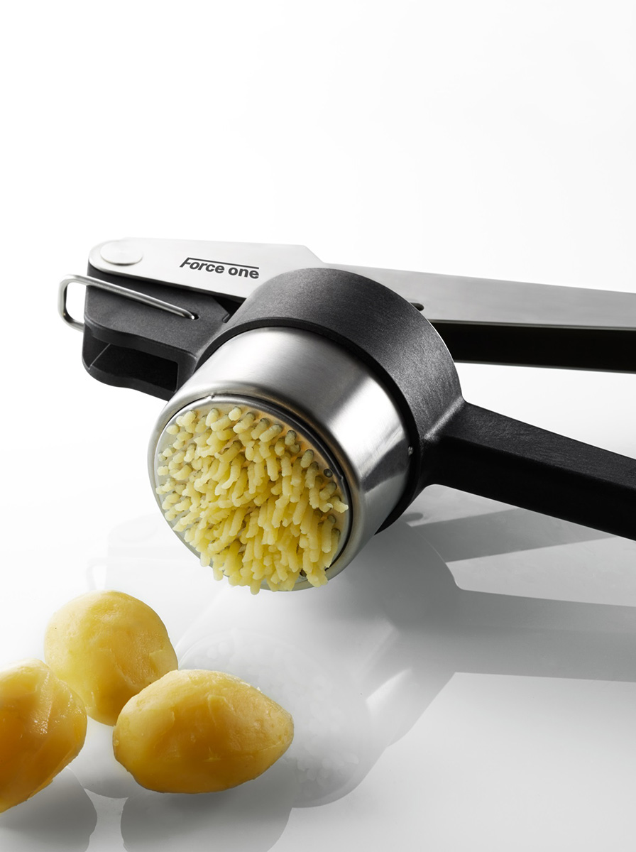 Kartoffelpresse mit frisch gepresstem Kartoffelteig und drei geschälten Kartoffeln