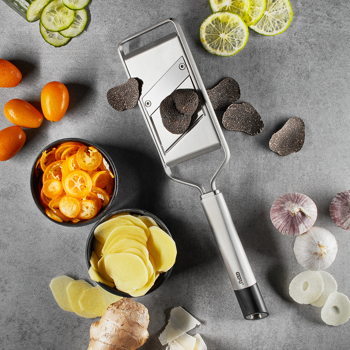 Edelstahltrüffelhobel mit frischem Trüffel und Gemüse Ein Edelstahltrüffelhobel, umgeben von geschnittenem Trüffel, Zitrone, Gurke und Knoblauch auf einer Küchenarbeitsplatte.