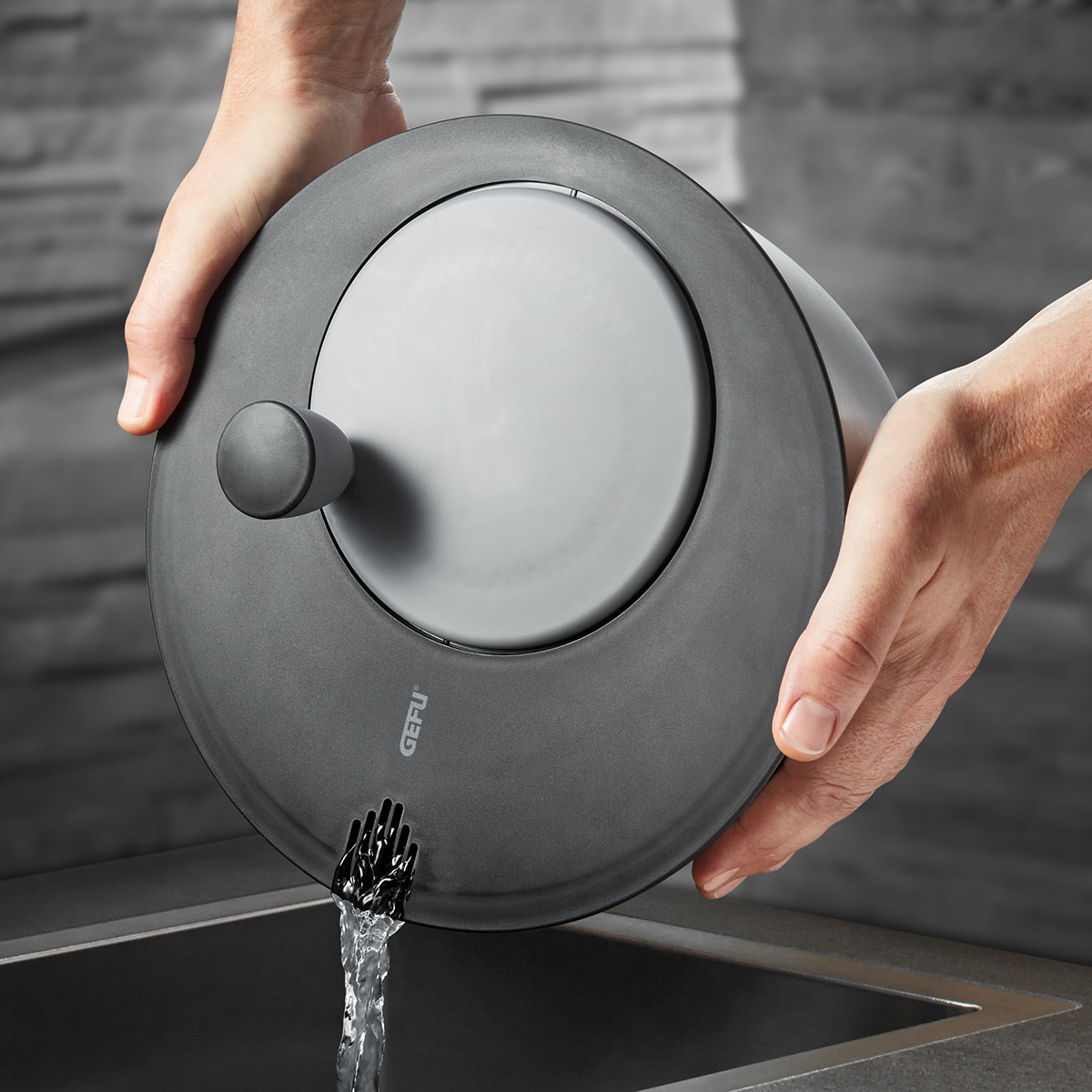 Moderner Wasserkocher beim Ausgießen von Wasser in die Spüle Hände halten einen grauen Wasserkocher, der in eine Spüle gießt