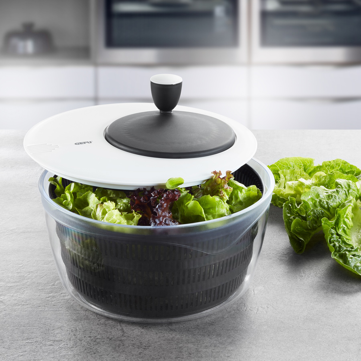 Praktische Salatschleuder mit frischem Salat auf Küchentisch Salatschleuder mit frischem Salat in einer modernen Küche auf dem Tisch befindlich