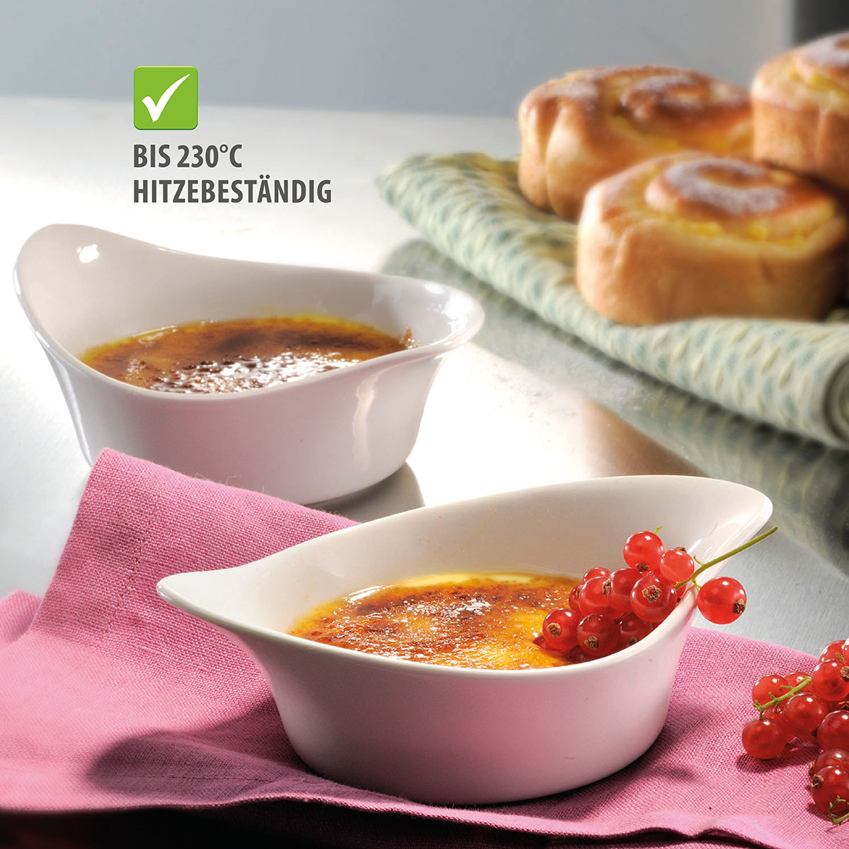 Zwei weiße Schalen mit Crème Brûlée auf einem rosa Tuch, dekoriert mit Johannisbeeren, hitzebeständig bis 230°C.