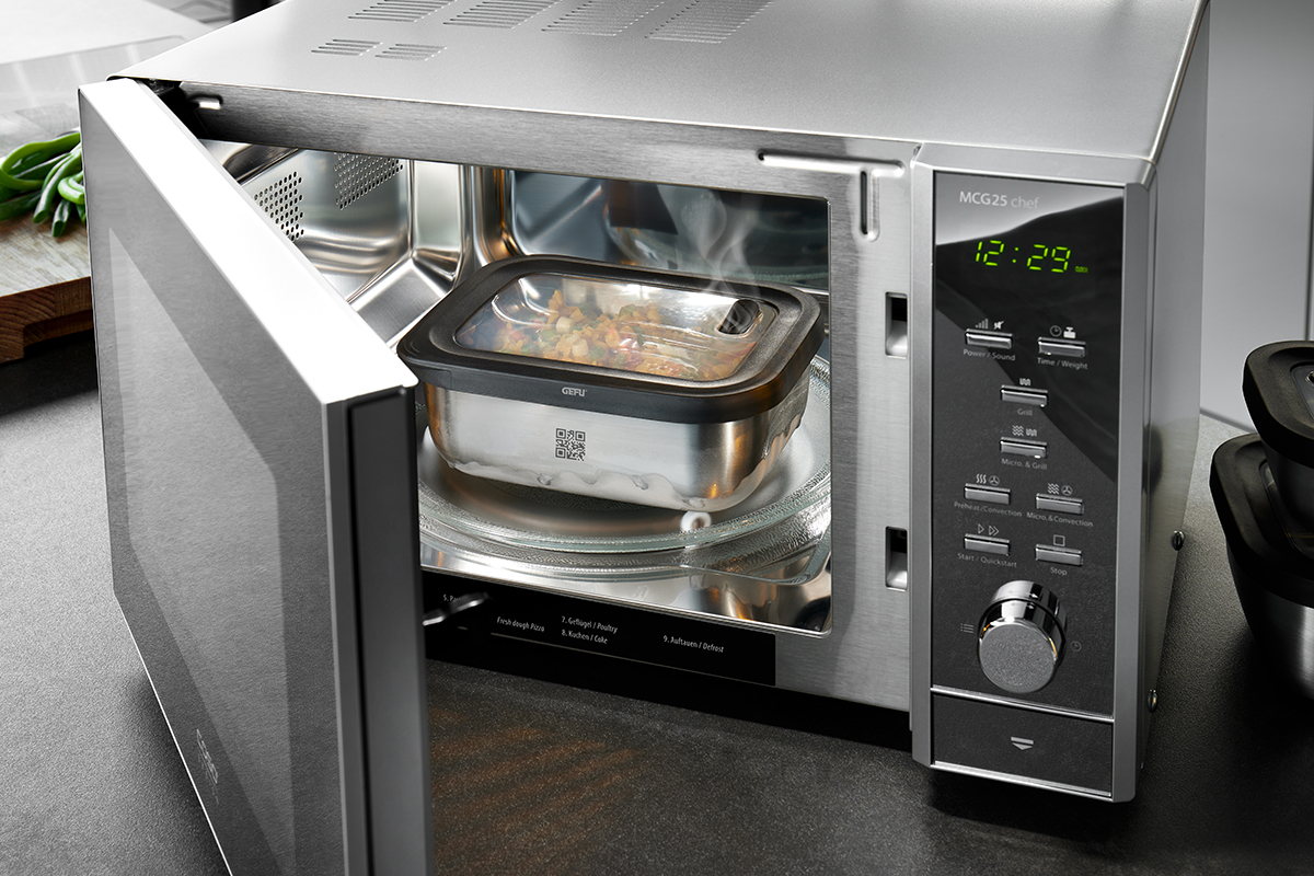 Moderne Mikrowelle mit geöffnetem Garraum und dampfendem Essen Eine geöffnete Mikrowelle zeigt dampfendes Essen in einem Behälter. Das Gerät verfügt über ein modernes Design und eine digitale Anzeige.