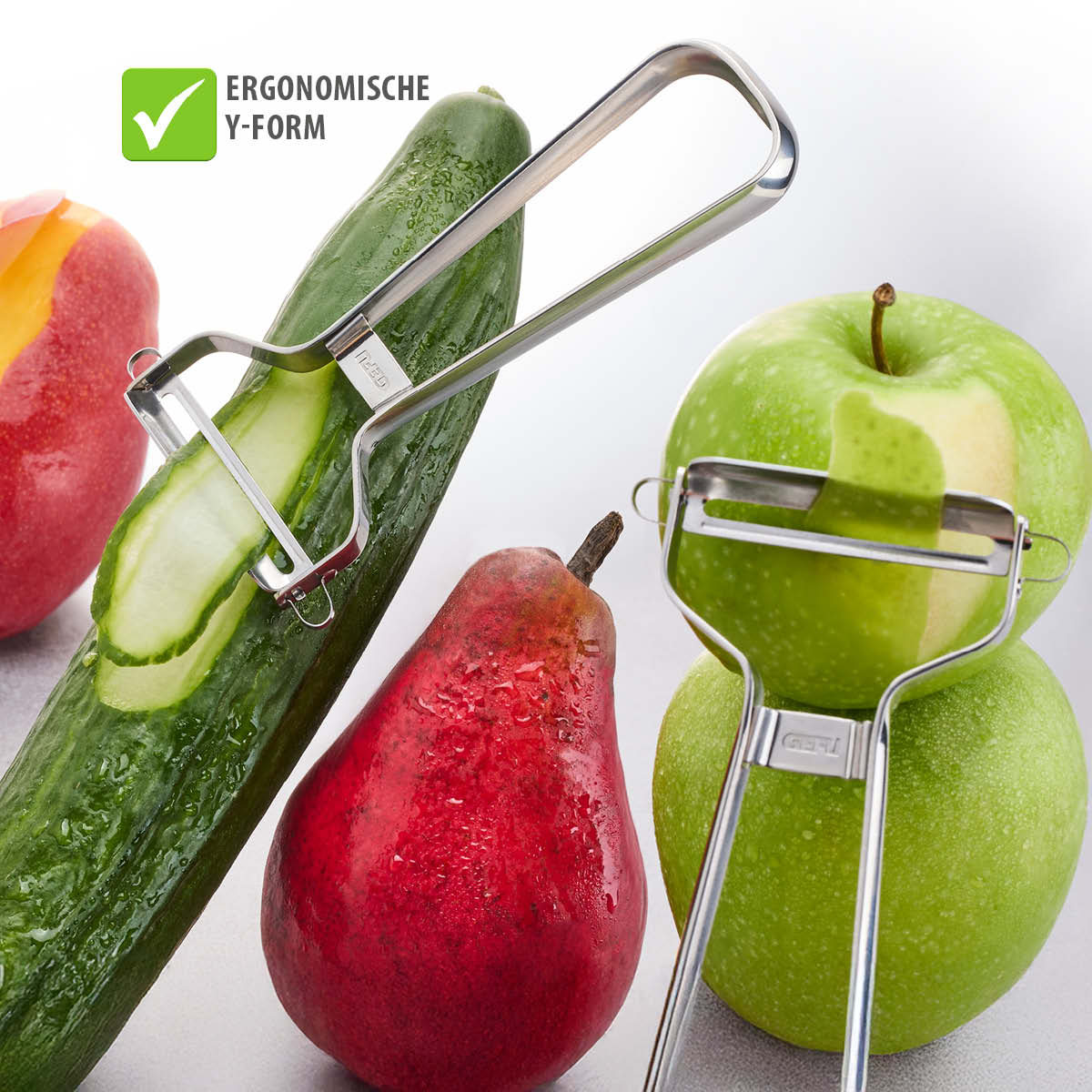 Zwei ergonomische Schäler in Y-Form, die Gurken und Äpfel schälen, umgeben von frischem Obst und Gemüse
