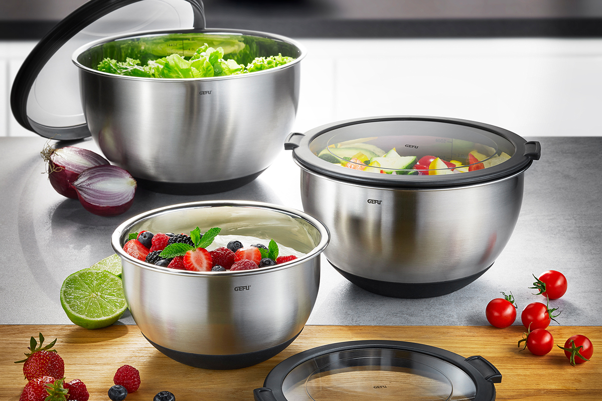 Edelstahl-Schüsseln mit Deckel für Lebensmittelaufbewahrung Drei Edelstahlschüsseln mit unterschiedlichen Lebensmitteln gefüllt: Salat, frisches Obst und Gemüse, mit Deckeln auf einer Küchenarbeitsplatte.