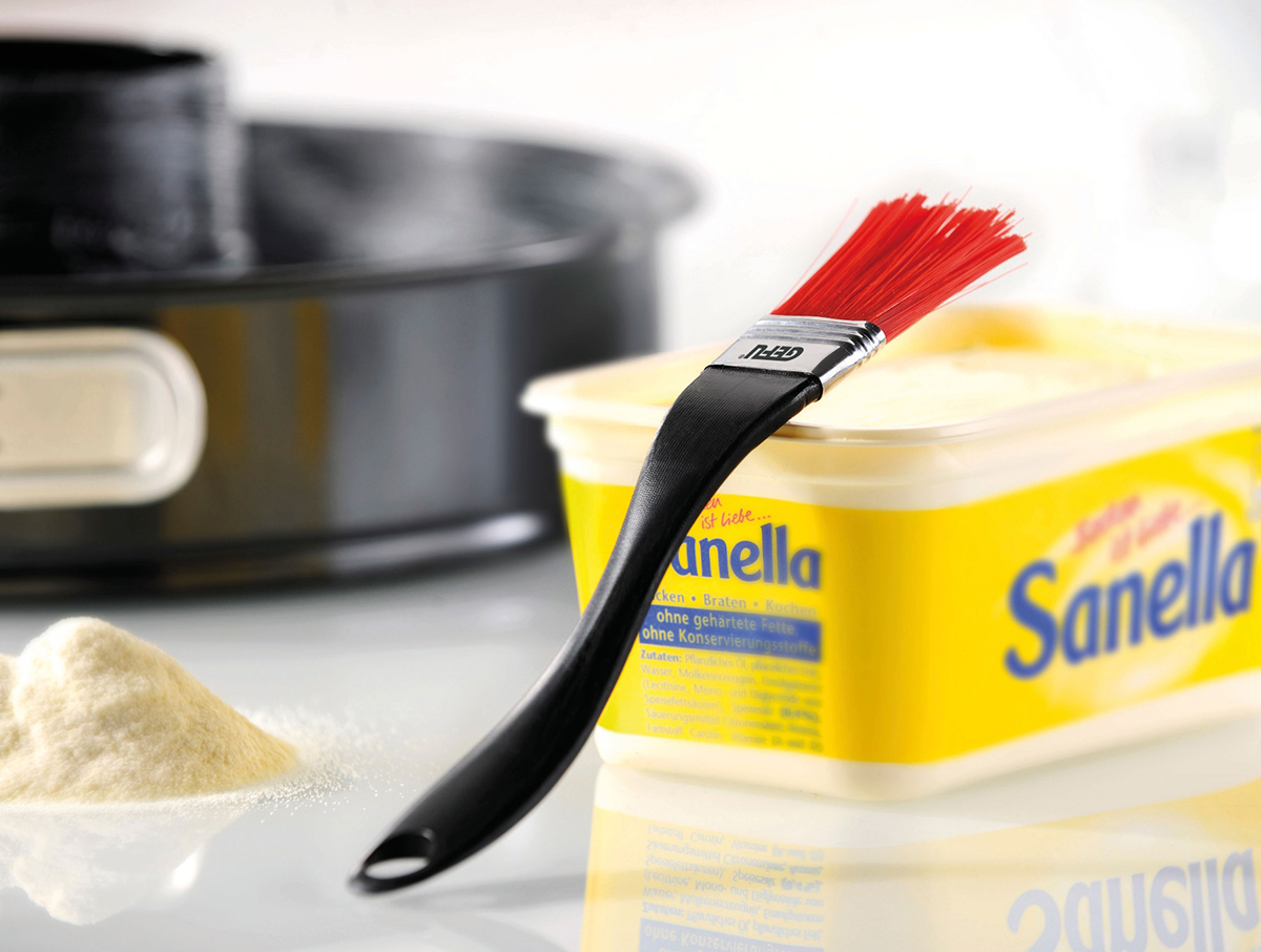 Backzubehör: Sanella Margarine mit Pinsel und Backform Nahaufnahme von Sanella Margarine mit rotem Pinsel und Backform im Hintergrund