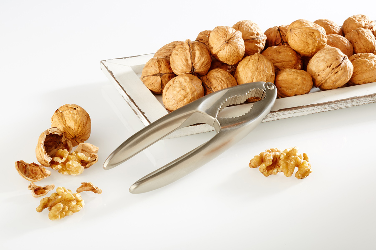 Edelstahl Nussknacker und Walnüsse auf weißem Untergrund Ein Nussknacker aus Edelstahl neben einer Schale voller Walnüsse, einige geknackt auf weißem Untergrund