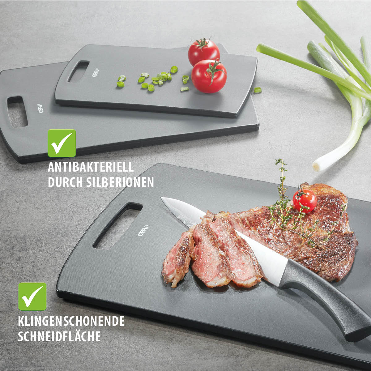 Antibakterielle Schneidebretter mit klingenschonender Oberfläche Drei graue Schneidebretter mit Silberionen-Beschichtung, darauf frisches Fleisch, Tomaten und Frühlingszwiebeln. Antibakteriell und klingenschonend.