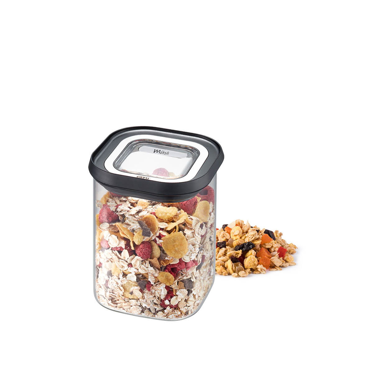 Transparente Müslidose mit schwarzem Deckel, gefüllt mit Müsli Eine quadratische, transparente Vorratsdose mit schwarzem Deckel, gefüllt mit Frühstücksmüsli, daneben lose Müslistücke auf weißem Hintergrund.