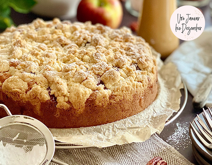 Apfelstreuselkuchen mit Pekannüssen und Karamellsauce Ein frisch gebackener Apfelstreuselkuchen, umgeben von Zutaten wie Äpfeln und Puderzucker, perfekt für jede Jahreszeit