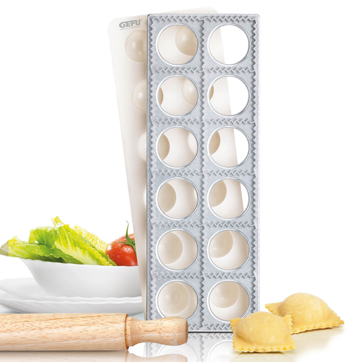 Raviolimaker mit Gemüse und Nudelholz Ravioli-Hersteller aus Metall, umgeben von knackigem Salat und einem Nudelholz