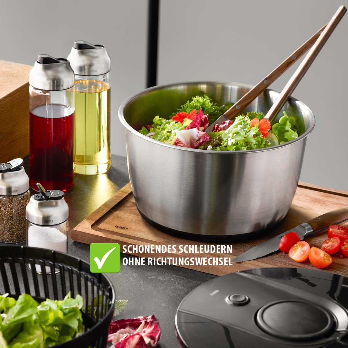 Edelstahl-Salatschüssel mit Schonendem Schleudermechanismus Edelstahl-Salatschüssel mit Salat, neben Essig- und Ölspendern sowie Gewürzstreuern