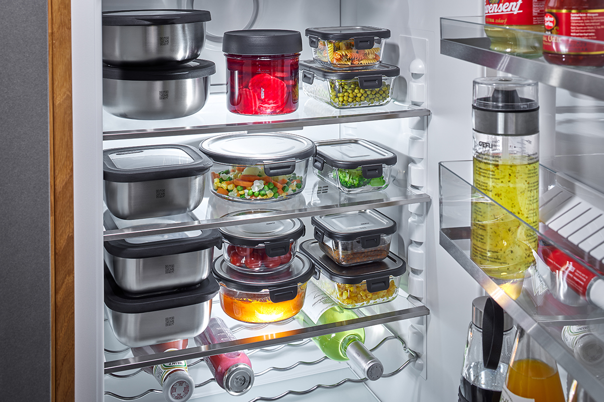 Vorratsbehälter im Kühlschrank zur optimalen Lebensmittelaufbewahrung Gefüllte Vorratsbehälter in verschiedenen Größen in einem Kühlschrank, umgeben von Flaschen.
