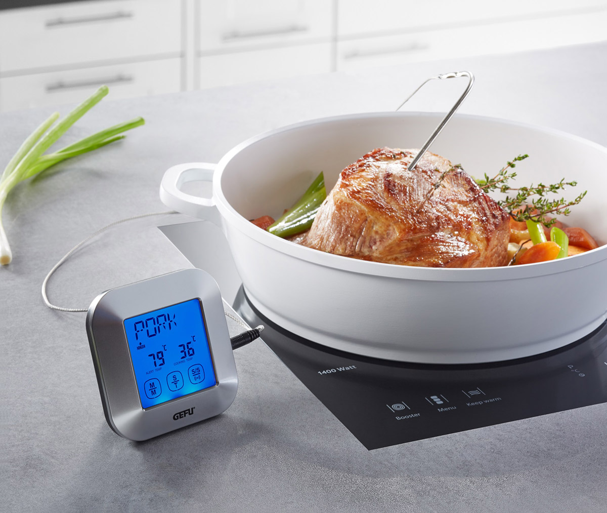 Digitales Fleischthermometer zeigt Temperatur eines Bratens in einem weißen Topf auf einem Herd an, umgeben von Gemüse.