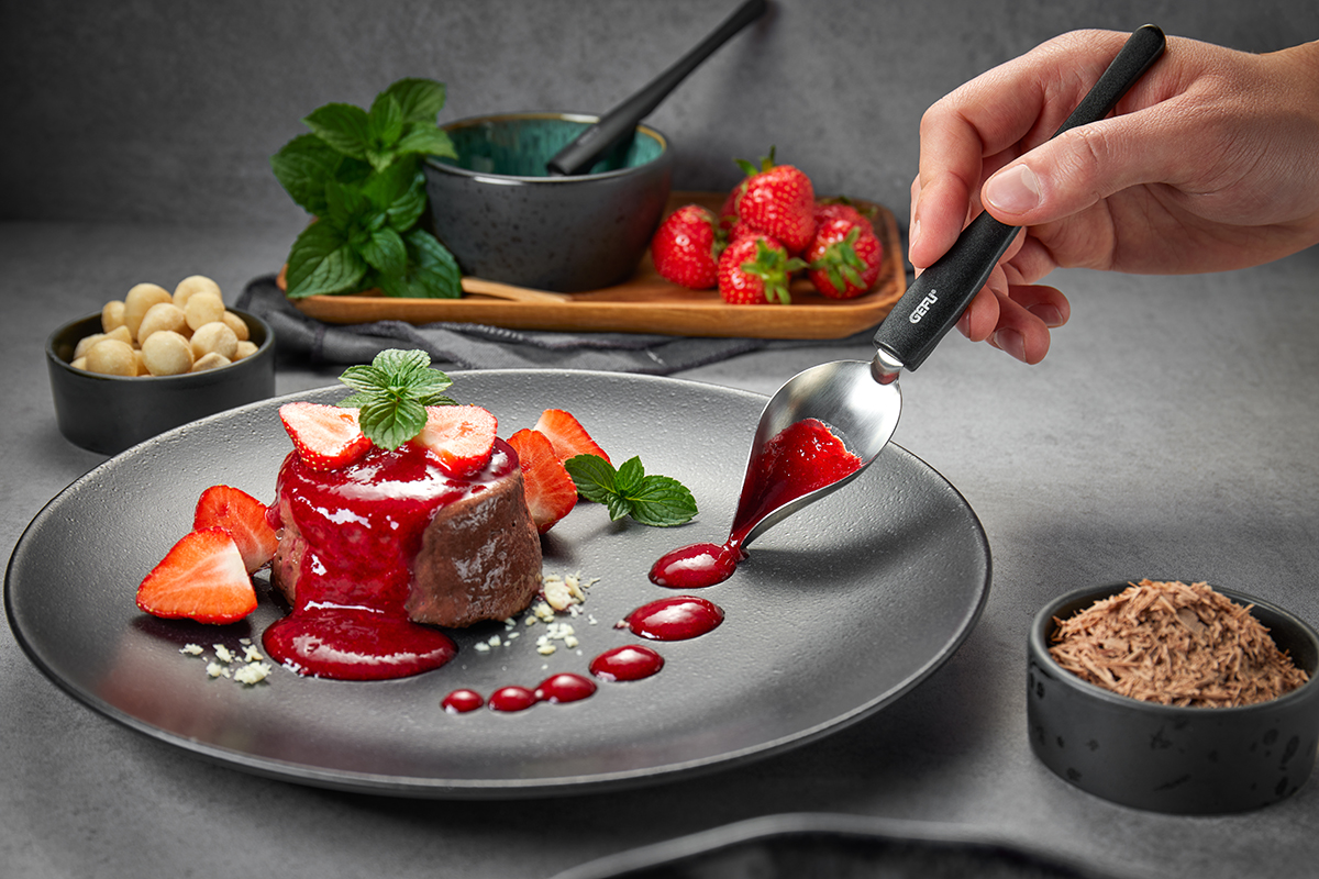 Schokoladendessert mit Erdbeersoße und frischen Erdbeeren Nahaufnahme eines Desserts aus Schokolade, garniert mit Erdbeersoße und frischen Erdbeeren auf einem grauen Teller