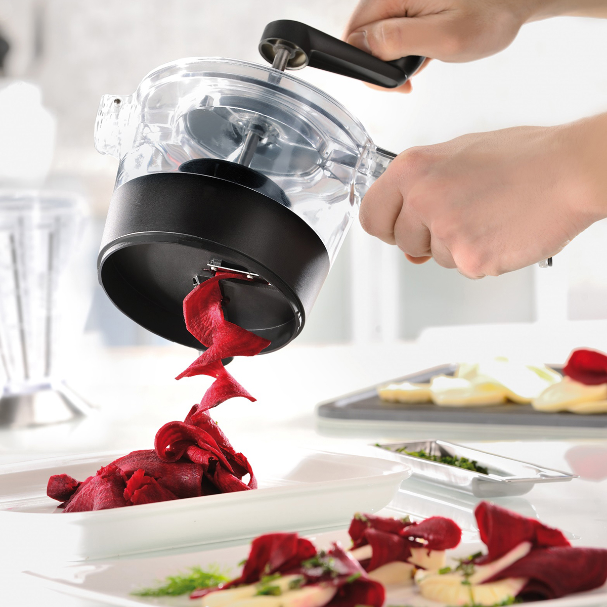 Praktische manuelle Küchenreibe beim Schneiden von roter Bete Manuelle Küchenreibe schneidet rote Bete in dekorative Streifen auf einem weißen Teller