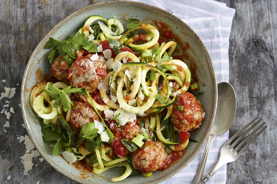 Bunte Zoodles mit Hackfleischklösschen  Ein Teller mit Zucchininudeln, Fleischbällchen und Tomatensauce, garniert mit Parmesan und frischen Kräutern