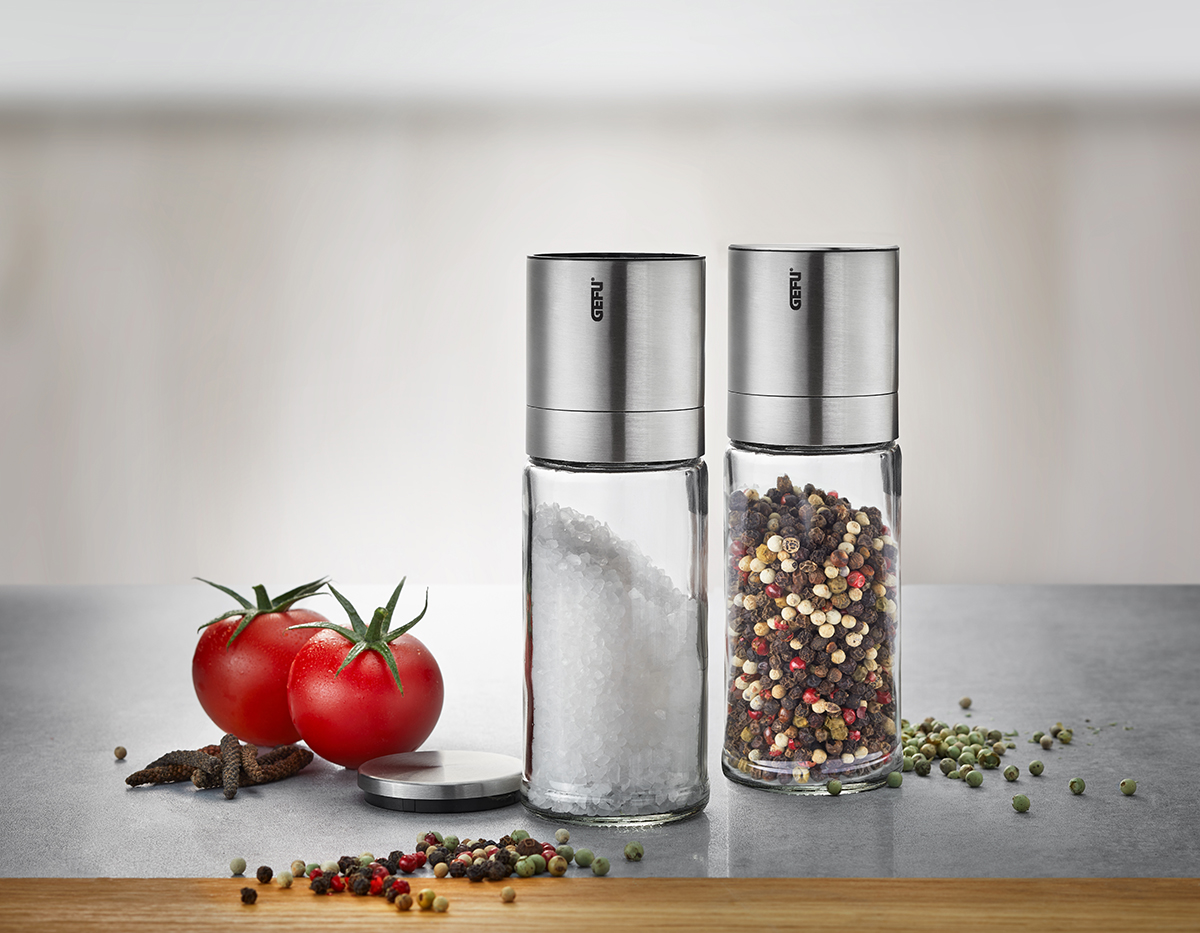Salz- und Pfeffermühle aus Edelstahl neben Tomaten auf einem Küchentisch