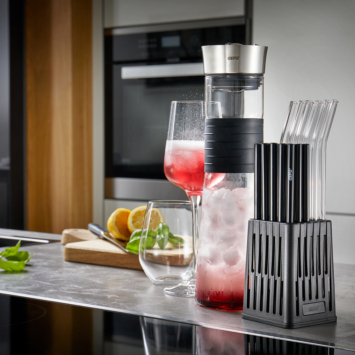 Stilvolle Trinkgläser und Karaffe mit erfrischendem Getränk in moderner Küche Eine Karaffe mit rosa Getränk und Eis, daneben Gläser und wiederverwendbare Trinkhalme in einer modernen Küchenszene.