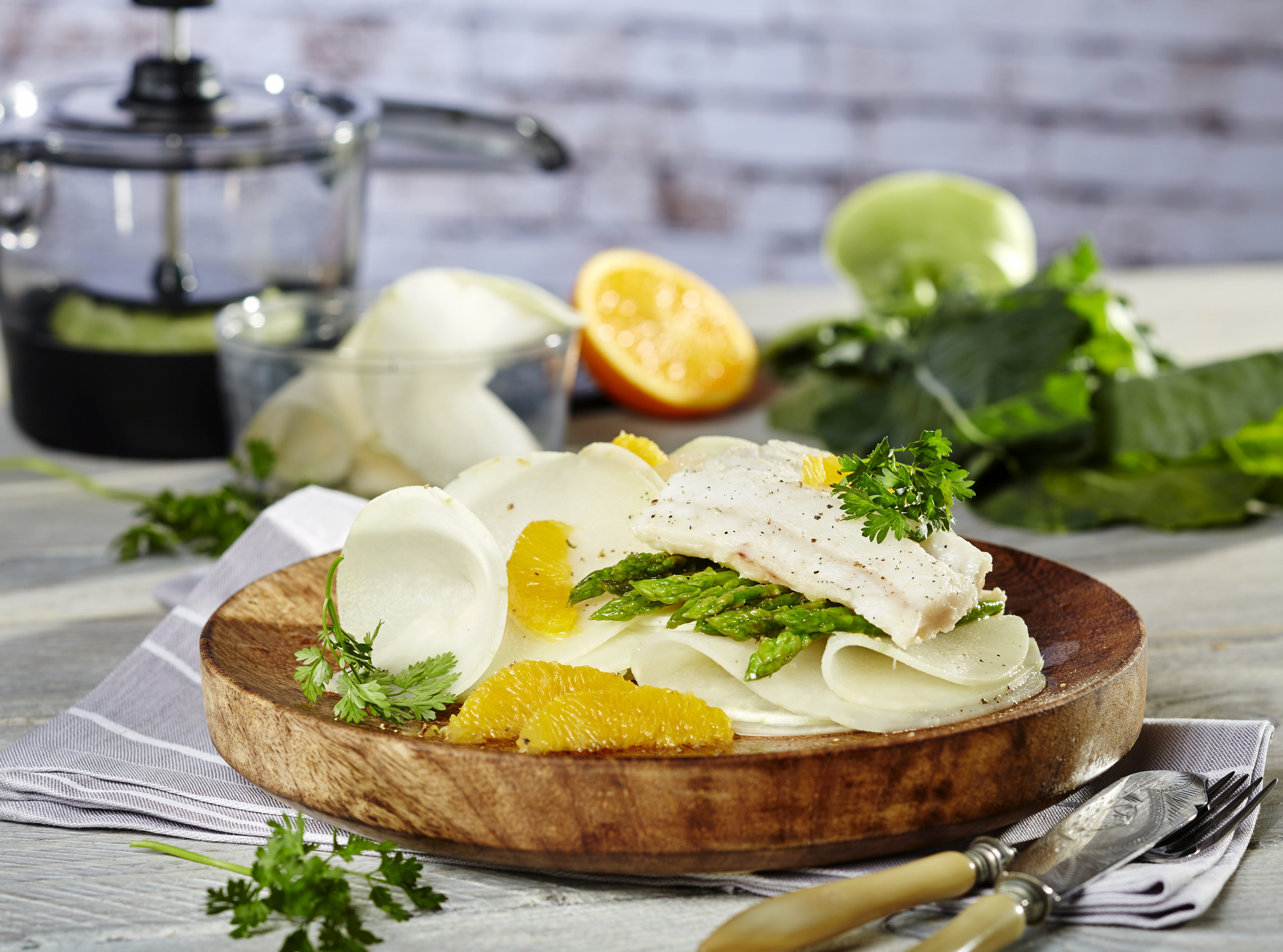 Confierter Kabeljau auf lauwarmem Kohlrabi-Spargel-Gemüse Ein gesunder Salat aus Spargel, Fischfilet und Orangenscheiben, kunstvoll angerichtet auf einem Holzteller, mit frischer Petersilie garniert, im Hintergrund verschiedene frische Zutaten