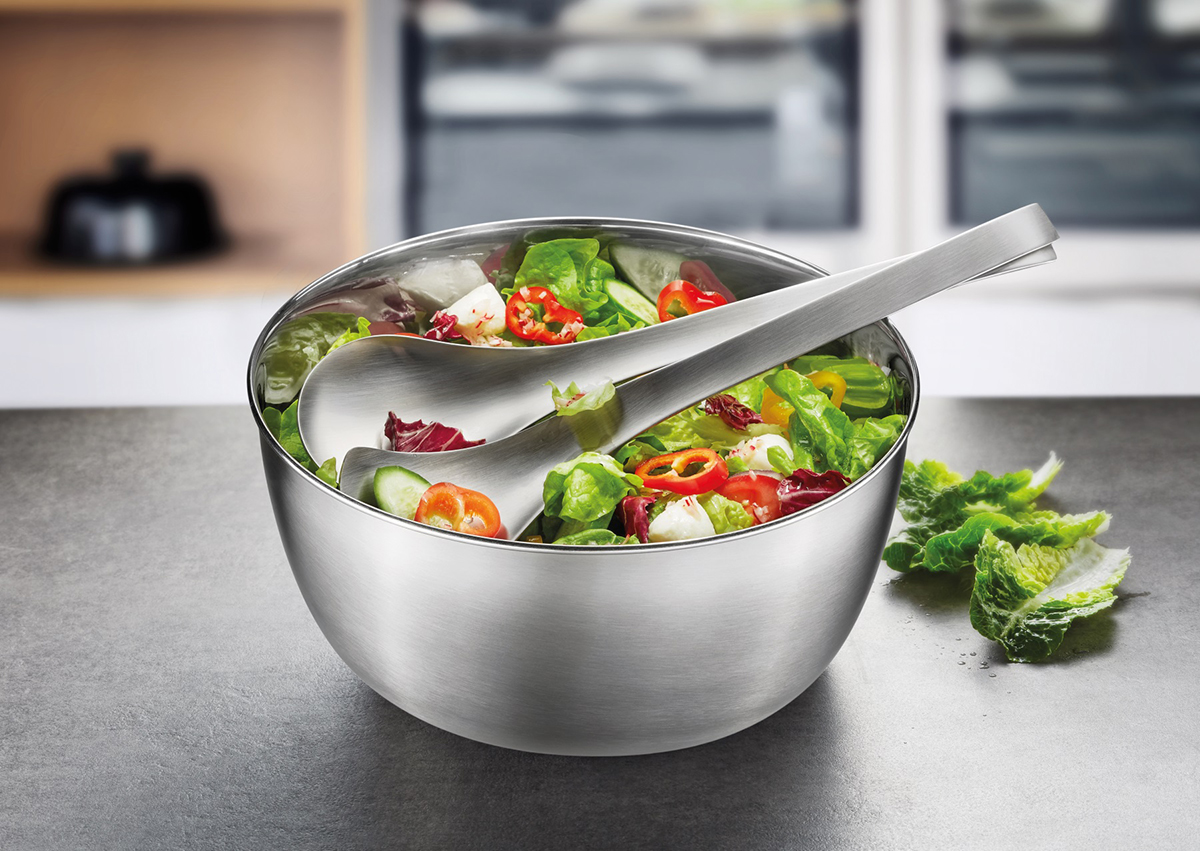 Elegante Edelstahlschüssel mit frischem Salat und Servierbesteck Edelstahlschüssel mit buntem Salat und Servierlöffel auf einem Tisch