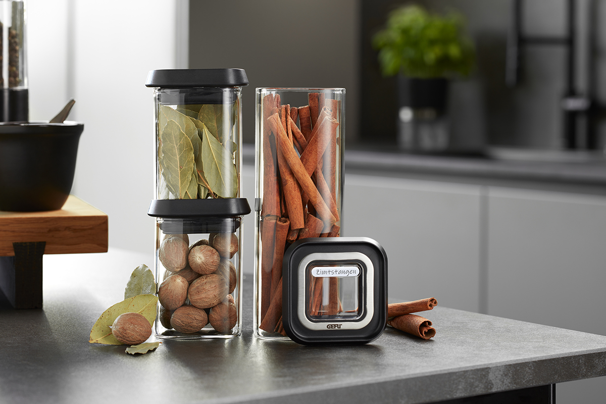 Stilvolle Gewürzgläser mit Lorbeerblättern, Muskatnüssen und Zimtstangen in moderner Küche Zwei Gewürzgläser mit Lorbeerblättern, Muskatnüssen und Zimtstangen auf einer Küchentheke