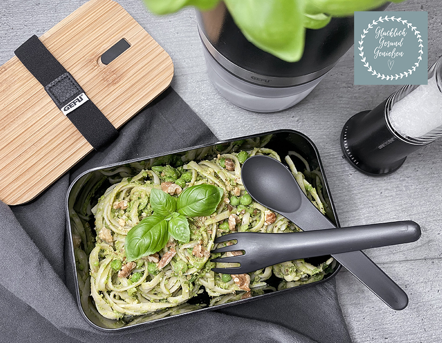 Erbsen-Pesto Spaghetti mit Erbsen und Basilikum in einer schwarzen Bento-Box, dazu schwarzes Besteck und ein Bambusdeckel auf grauem Untergrund
