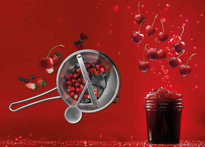 Manuelle Beerenpresse mit roten Beeren und Marmeladenglas auf rotem Hintergrund