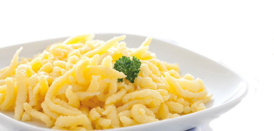 Frische Spätzle auf weißem Teller mit Petersiliengarnitur Nahaufnahme von frischen Spätzle auf einem weißen Teller, dekoriert mit einem Zweig Petersilie, vor weißem Hintergrund.