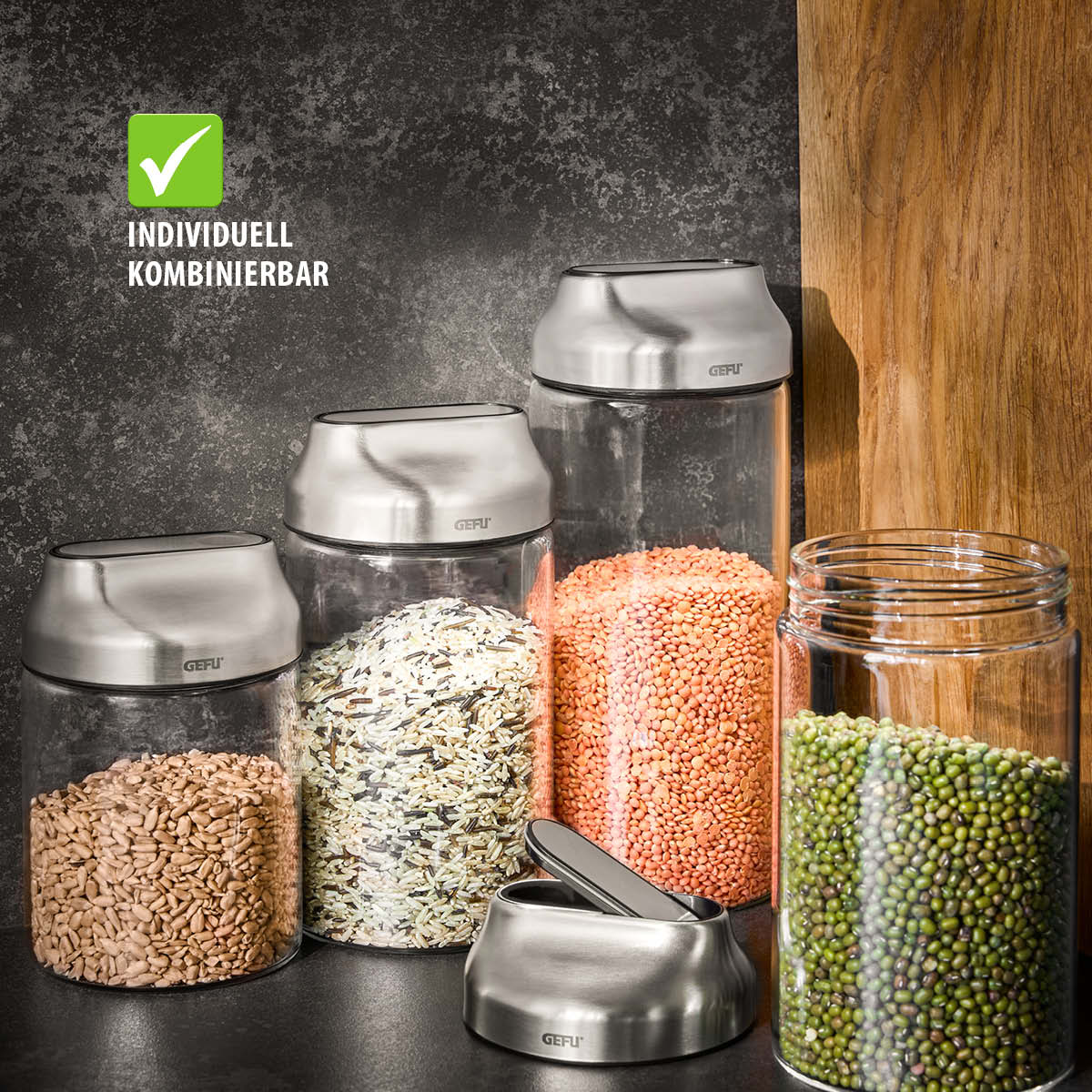 Stilvolle Glasbehälter mit Edelstahldeckeln für individuelle Kombinationen Vier Glasbehälter mit Edelstahldeckeln, gefüllt mit Linsen, Reis und anderen Körnern, auf dunklem Hintergrund und Holzunterlage, individuell kombinierbar