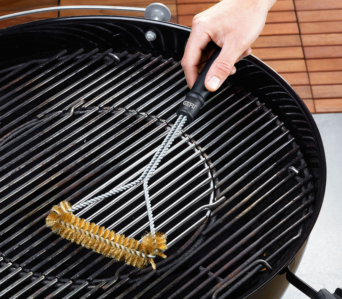 Grillbürste mit ergonomischem Griff für effektive Reinigung Person reinigt einen Grillrost mit einer stabilen Grillbürste aus Metall.