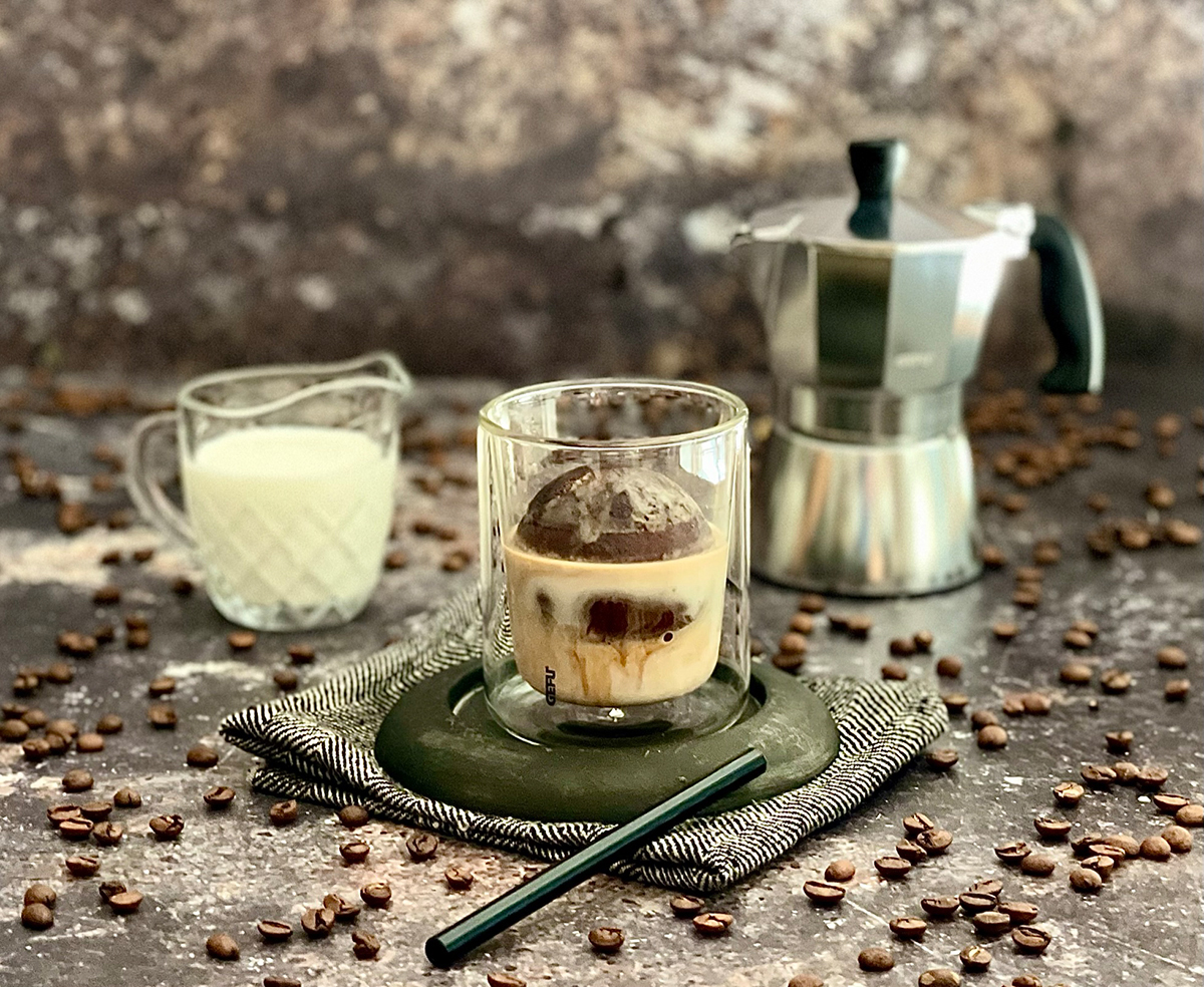 Affogato mit Kaffeemaschine und Milch auf Holztisch Nahaufnahme eines Affogato-Getränks, umgeben von Kaffeebohnen, einer Espressomaschine und einem Glas Milch auf einem rustikalen Tisch