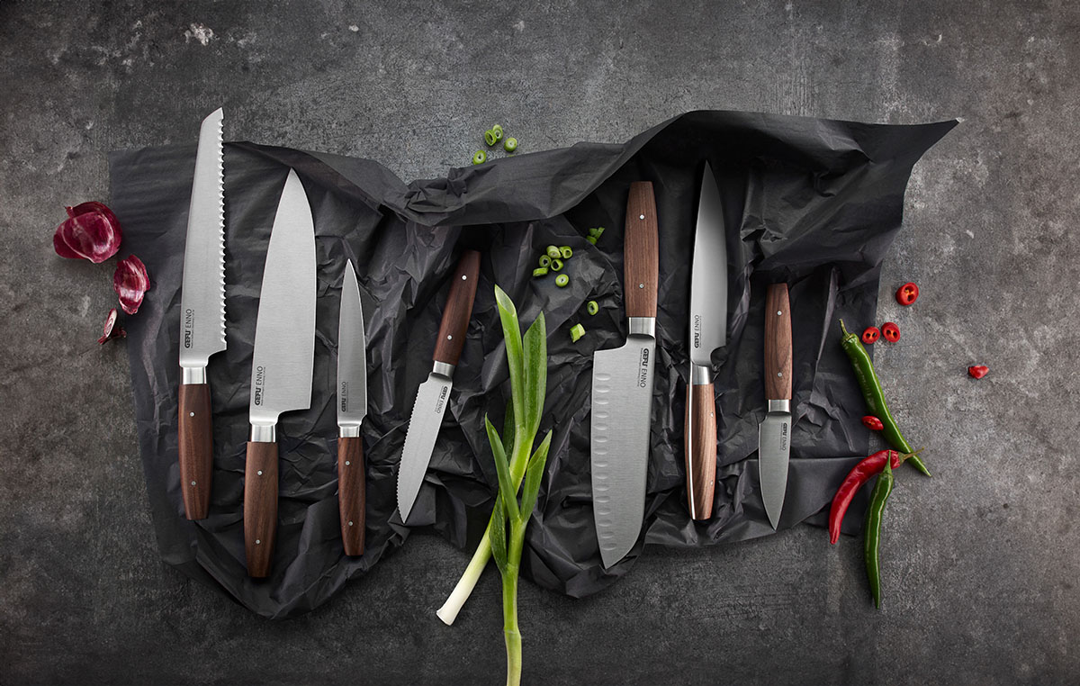 Hochwertiges Messerset mit Holzakzenten und frischem Gemüse Ein Sortiment scharfer Küchenmesser mit Holzgriffen, umgeben von Frühlingszwiebeln, roten Zwiebeln und Chilischoten auf dunklem Hintergrund