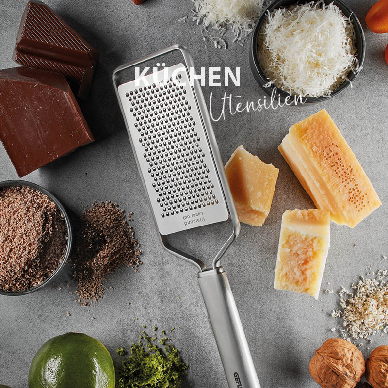 Küchenreibe auf einem Tisch mit geriebenem Käse, Schokolade, Limetten und Nüssen