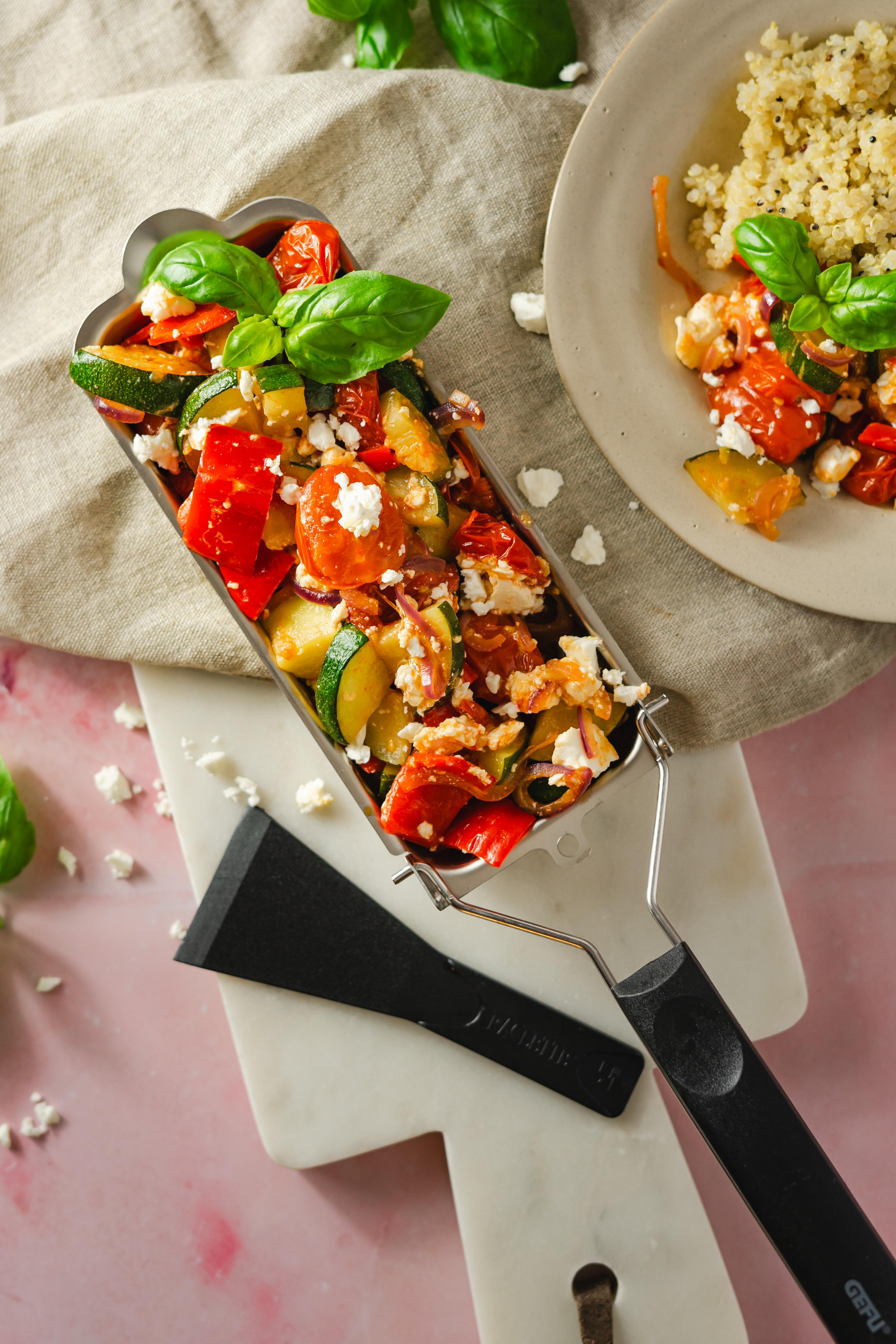 Mediterranes Grillgemüse Ein Ofengericht mit buntem Gemüse, Feta und frischem Basilikum, serviert auf einem weißem Marmorschneidebrett, daneben ein Teller mit Quinoa.